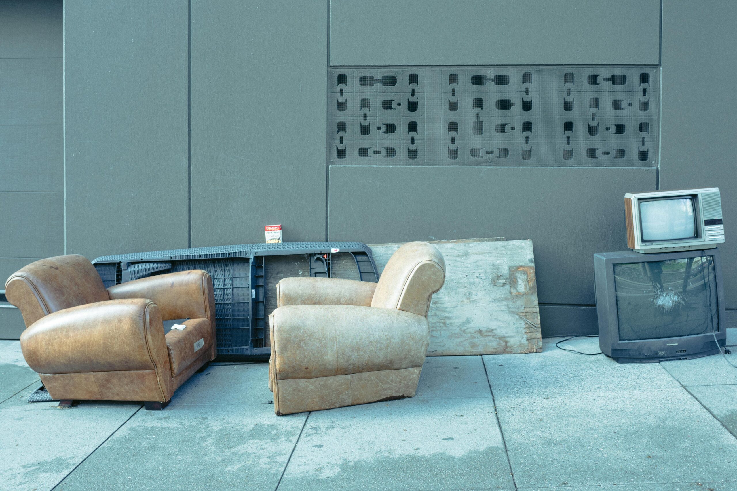 Sidewalk scene with vintage chairs and old televisions against a wall.